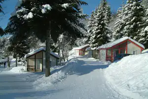 Campinghäuser im Schnee mit verschneiten Dächern, Bäumen und einem Weg auf dem Campingplatz.