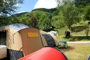 Zelte auf einem Campingplatz im Grünen, mit Tisch und Bänken am Stellplatz, umgeben von Bäumen und Hügeln.