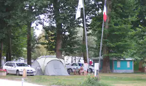 Zelt auf dem Campingplatz unter hohen Bäumen, daneben Autos und ein Tisch mit Stühlen.