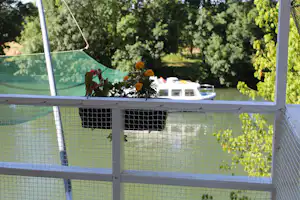 Blumen auf dem Balkon mit Blick in den Garten, im Hintergrund ein Boot und Bäume hinter dem Zaun.