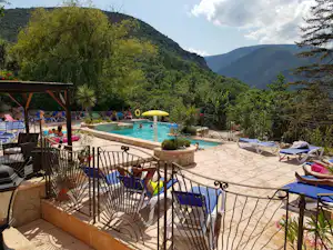 Pool auf der Terrasse eines Campingplatzes mit Sonnenliegen, Blick auf grüne Berge und Bäume.