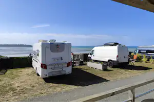 Wohnmobile auf einem Stellplatz am Meer, mit Blick auf Wasser und Küste, neben einem Holzgeländer.