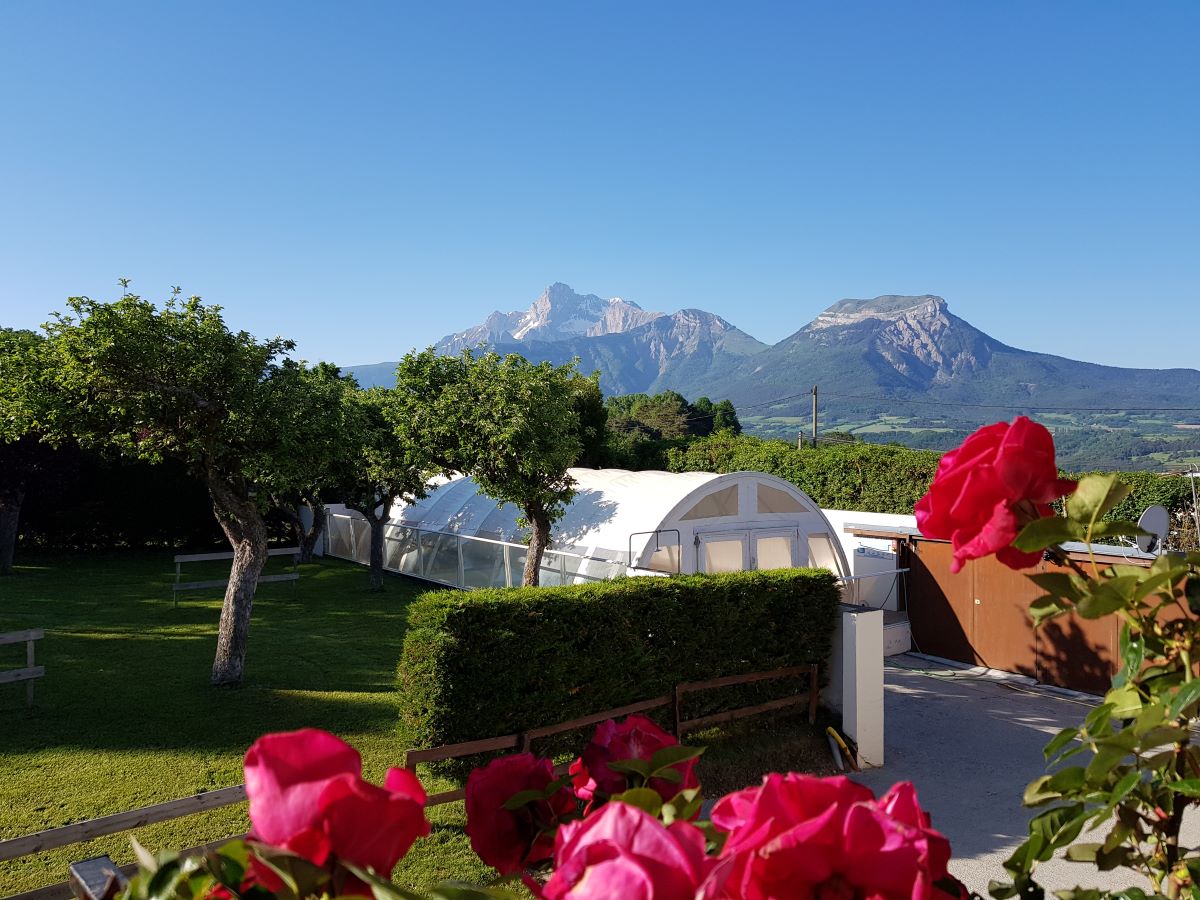 Weiße Zelte auf einem Campingplatz, umgeben von Bäumen und Hecken, mit Bergblick im Hintergrund.