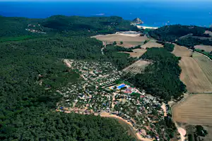 Luftaufnahme eines Campingplatzes mit Pool, vielen Stellplätzen und Wegen im Grünen, nahe dem Meer und einem kleinen Strand.