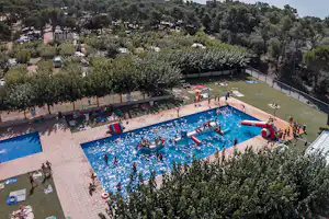 Großes Camping-Schwimmbad mit aufblasbaren Spielgeräten, Liegewiese und vielen Gästen, umgeben von Olivenbäumen und Stellplätzen.