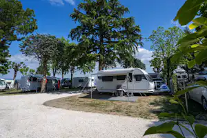 Wohnwagen auf einem Campingplatz zwischen Bäumen, mit Vorzelt und Sitzbereich, im Hintergrund weitere Wohnmobile.