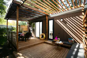 Holzterrasse am Campinghaus mit Sitzgruppe, Tisch und Sonnenschirm, daneben ein Holzschuppen und Gartenzaun.