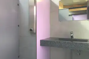 Innenansicht eines modernen Badezimmers mit grauem Waschbecken, Spiegel und Handtuchhalter, daneben eine Tür und Wandpaneele.
