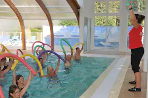 Überdachtes Schwimmbecken im Campinghaus, Kinder und Erwachsene im Wasser mit bunten Spielreifen, große Fensterfront.