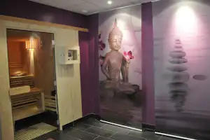 Sauna mit Holzbank und Buddha-Wandbild, Fliesenboden und beleuchtetem Innenraum im Wellnessbereich.