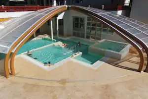 Beheiztes Poolbecken mit türkisfarbenem Wasser unter einer transparenten Überdachung, am Rand Liegen und Sitzbereiche.