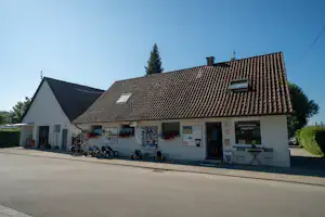 Rezeption eines Campingplatzes: weißes Gebäude mit Schindeldach, Aushangtafeln und Fahrrädern vor dem Eingang.