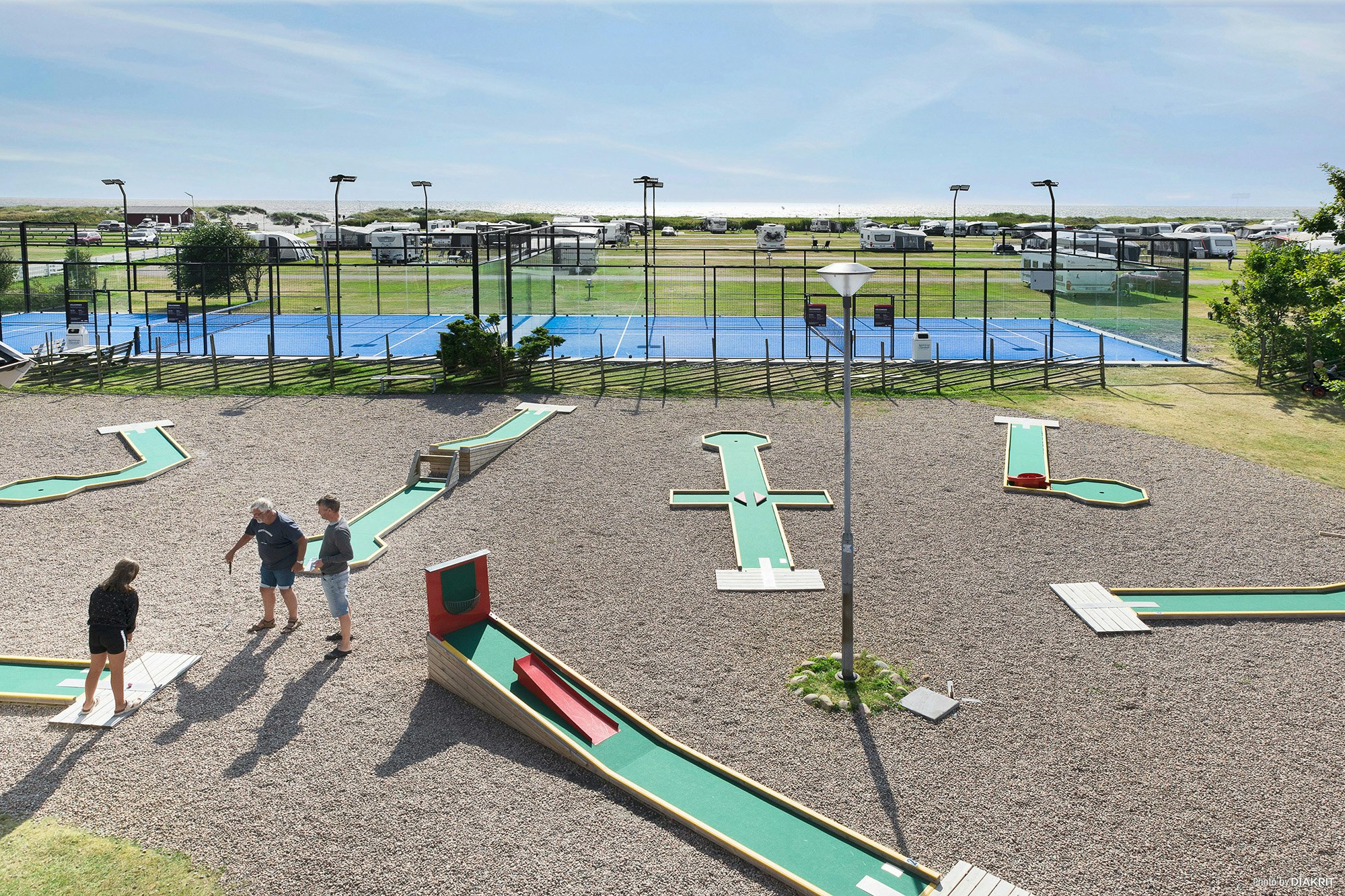 Minigolfanlage auf dem Campingplatz mit grünen Bahnen, Bäumen und mehreren Wohnmobilen im Hintergrund.
