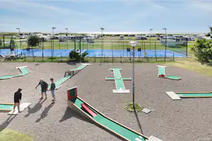 Minigolfanlage auf dem Campingplatz mit grünen Bahnen, Bäumen und mehreren Wohnmobilen im Hintergrund.