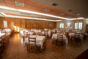 Speisesaal im Campingbereich mit vielen Tischen und Stühlen, Fliesenboden und großen Fenstern.