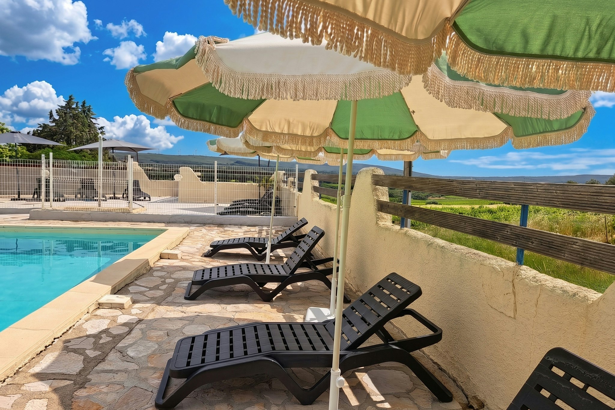 Sonnenliegen auf einer Terrasse am Campingplatz mit Blick auf den Pool und das Meer, neben Sonnenschirmen.