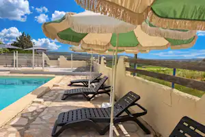 Sonnenliegen auf einer Terrasse am Campingplatz mit Blick auf den Pool und das Meer, neben Sonnenschirmen.