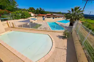 Großer Camping-Pool mit Zaun, daneben ein zweiter Pool, Gebäude und Rasenfläche im Hintergrund unter klarem Himmel.