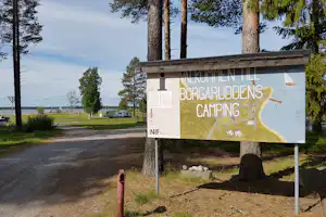 Camping Borgaruddens Havsbad - Willkommensschild und Einfahrt zum Campingplatz im Vordergrund, Wohnwagen- und Zeltstellplatz mit Blick aufs Meer im Hintergrund