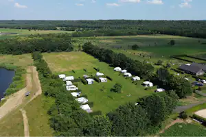 Luftaufnahme eines Campingplatzes mit mehreren Wohnwagen und Zelten auf einer Wiese, am Rand ein See und Wege.