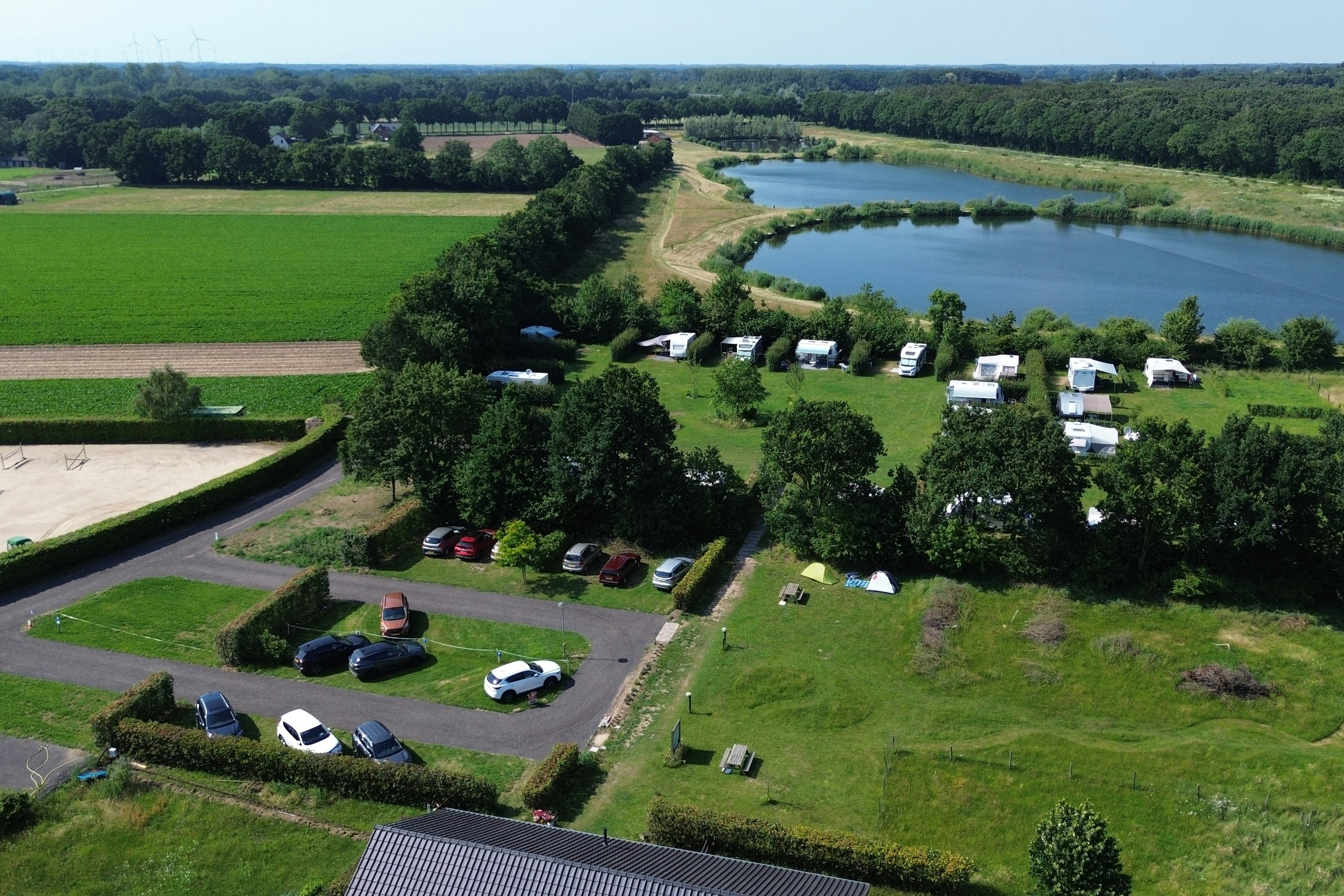 Luftaufnahme eines Campingplatzes mit Stellplätzen, Wohnwagen und Zelten, umgeben von Wiesen, Bäumen und einem nahegelegenen Fluss.