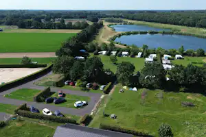 Luftaufnahme eines Campingplatzes mit Stellplätzen, Wohnwagen und Zelten, umgeben von Wiesen, Bäumen und einem nahegelegenen Fluss.