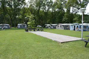 Rasenfläche mit befestigtem Weg und Sitzbank, im Hintergrund mehrere Zelte und Wohnwagen auf dem Campingplatz.