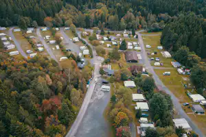 Luftaufnahme eines Campingplatzes im Wald mit Wohnwagen, Stellplätzen und breiten Wegen zwischen den Parzellen.