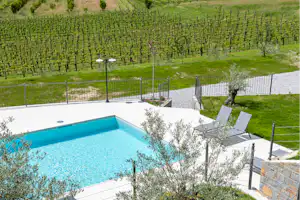 Blauer Pool auf einer Terrasse mit Blick auf einen gepflegten Garten und Weinberge im Hintergrund.