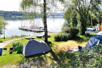 Camping Brugger am Riegsee  -  Zeltplatz vom Campingplatz zwischen Bäumen mit Blick auf die Anlegestelle und den See