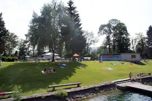 Campingwiese mit Liegen am Pool, umgeben von Bäumen, im Hintergrund Zelte und ein Gebäude.