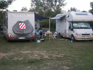 Zwei Wohnwagen und ein Wohnmobil auf einem Campingplatz mit Rasen, Markise, Stühlen und Tisch zwischen den Fahrzeugen.