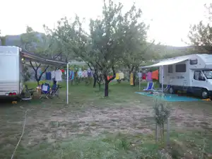 Zwei Wohnwagen auf einem Campingplatz zwischen Bäumen, mit Wäscheleine, Campingstühlen und einem kleinen Tisch am Stellplatz.