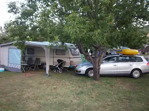 Wohnwagen und Zelt am Campingplatz unter einem Baum, daneben ein Auto und Campingstühle auf dem Rasen.