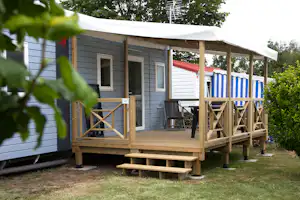 Holzveranda an einem Wohnwagen mit Stufen, Sitzbank und Grill auf dem Campingplatz, im Hintergrund weitere Wohnwagen.