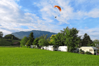 Camping Buosingen - Wohnwagen auf Stellplätzen mit einer Wiese davor und Paraglider in der Luft