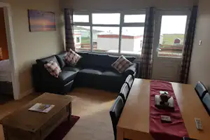 Wohnzimmer mit schwarzem Sofa, Holztisch und Esstisch am Fenster, Blick auf Häuser und Wiese.