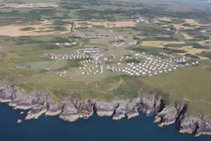 Luftaufnahme eines Campingplatzes an der Küste mit vielen Wohnwagen, Wegen und Feldern zwischen Felsen und Meer.