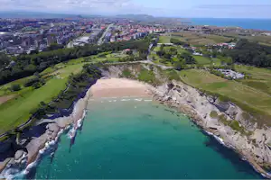Luftaufnahme eines Campingplatzes an einer felsigen Küste mit Sandstrand, türkisfarbenem Wasser und Parkplätzen am Hang.