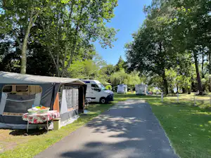 Zelt und Wohnwagen-Stellplatz am Campingplatz, daneben ein weißer Transporter und ein gepflegter Weg durch den Rasen.