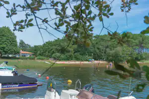 Bootssteg am See mit geparkten Motorbooten, Ruderbooten und Blick auf Ufer mit Bäumen und Häusern.