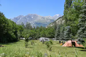 Campingwiese mit Zelt, Wohnwagen und Bäumen vor hohen Bergen im Hintergrund.