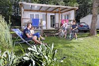 Campéole Le Giessen  -  Camper Familie auf grüner Wiese am Mobilheim vom Campingplatz mit Veranda