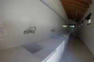 Modernes Camping-Badezimmer mit weißen Fliesen, Waschbecken, Armaturen und Dusche im Hintergrund.