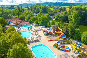 Blick auf den Campingplatz mit großem Pool, Kinderbecken und bunten Wasserrutschen, umgeben von Bäumen und Gebäuden.