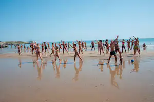 Gruppe von Badegästen steht im flachen Wasser am Strand, hebt die Arme und spielt am Meer.