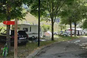 Wohnmobil und Auto auf dem Campingplatz, Zelt zwischen Bäumen, Stellplatzschilder mit Nummern und Weg am Rand.