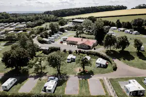 Luftaufnahme eines Campingplatzes mit Wohnwagen, kleinen Wegen, Bäumen und mehreren Gebäuden im grünen Gelände.