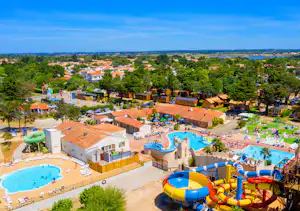 Blick auf Campinganlage mit beheiztem Pool, Wasserrutschen, Sonnenterrassen und vielen Bungalows zwischen Bäumen.
