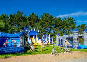 Blauer Hüpfburg-Spielplatz mit Rutsche, Trampolin und Fahrrad auf dem Rasen vor hohen Bäumen.